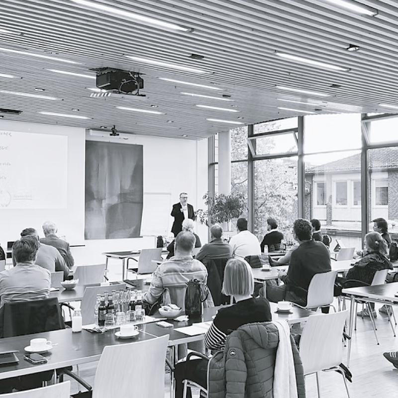 Schwarz-weiß Aufnahme eines gefüllten Seminarraums mit Blick auf Olaf Rosenbaum und die Teilnehmer.